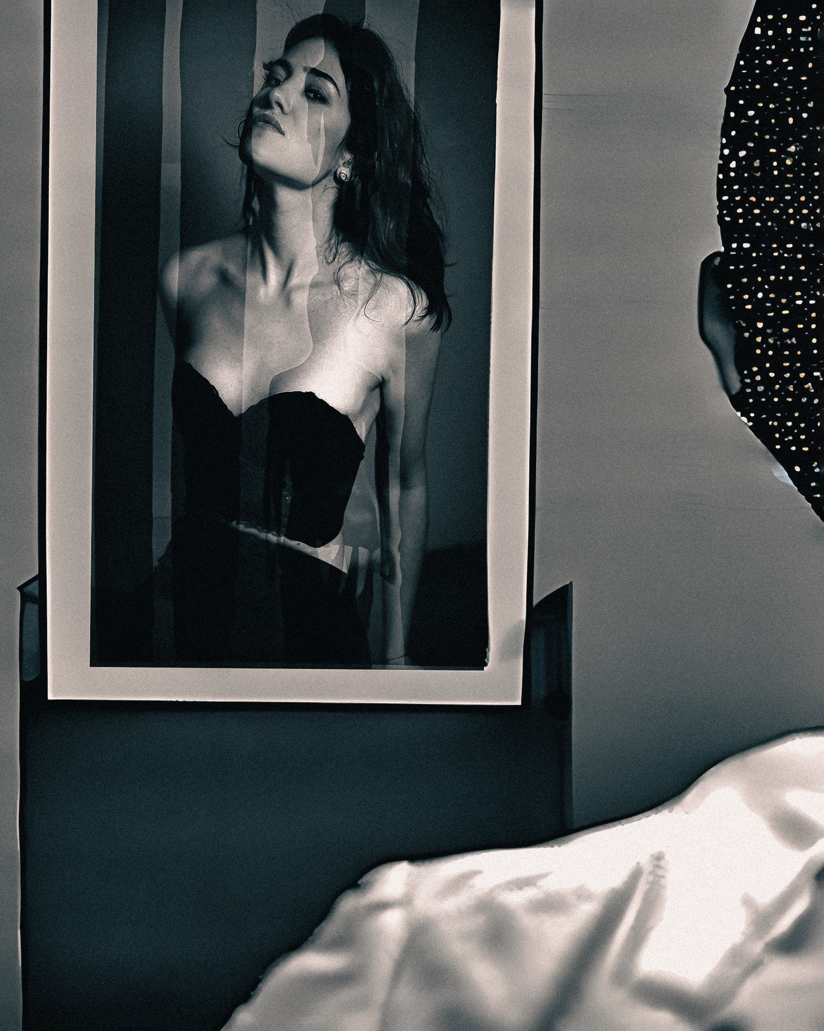 Black and white interior with a framed print of a woman in a strapless dress, sheets in the foreground — fine art by Hamudi Leon