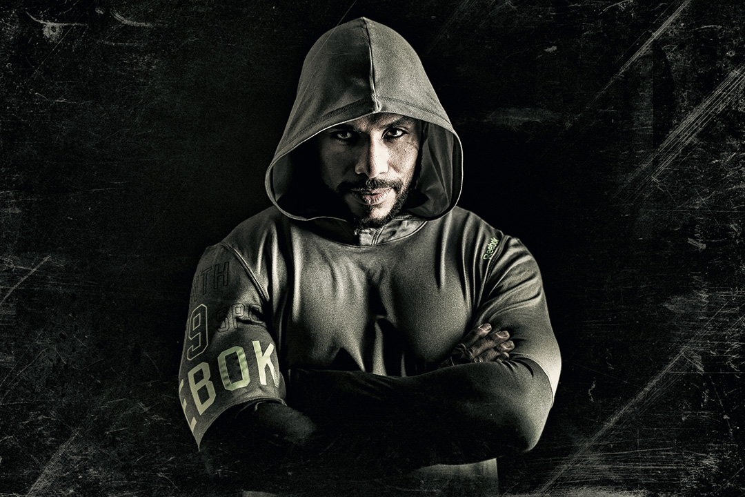 Athlete in a hooded sweatshirt, arms folded, facing the camera against a dark scratched wall — sports photograph by Hamudi Leon