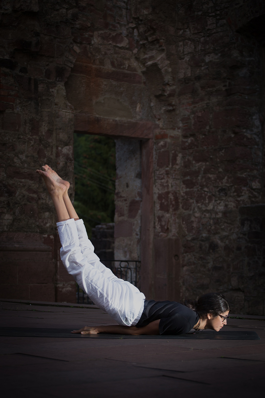 Woman holding a raised-leg yoga pose on a mat in the doorway of a stone ruin — sports photograph by Hamudi Leon