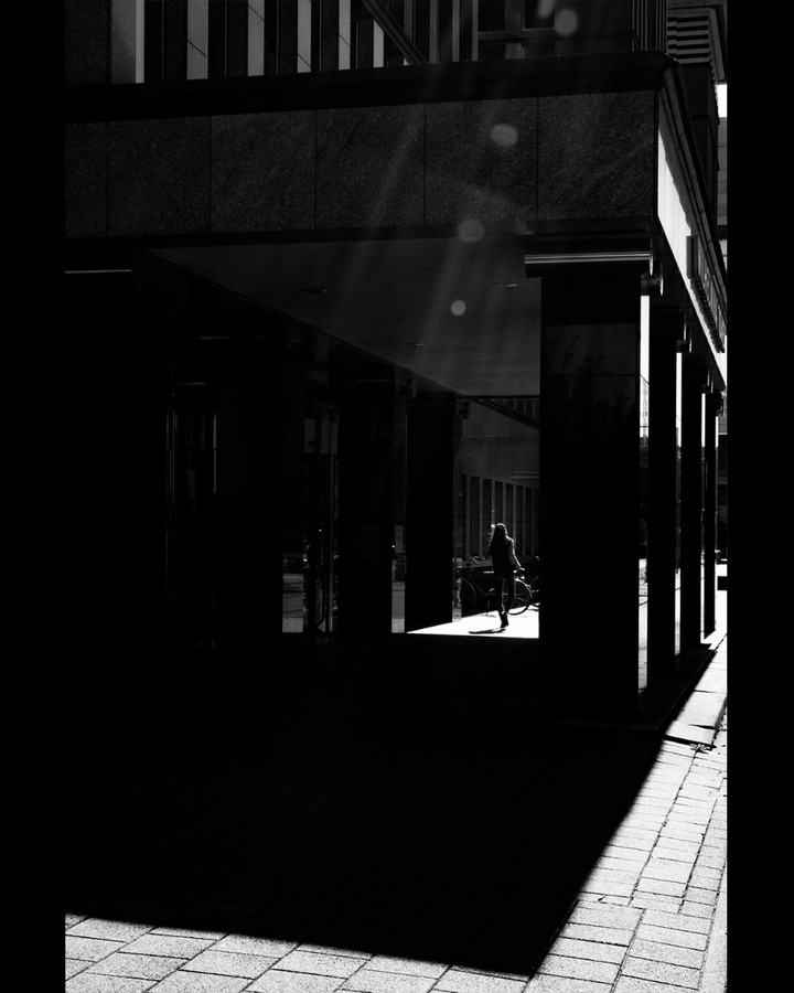 Long dark arcade with a single sunlit figure at the far end — street photograph by Hamudi Leon