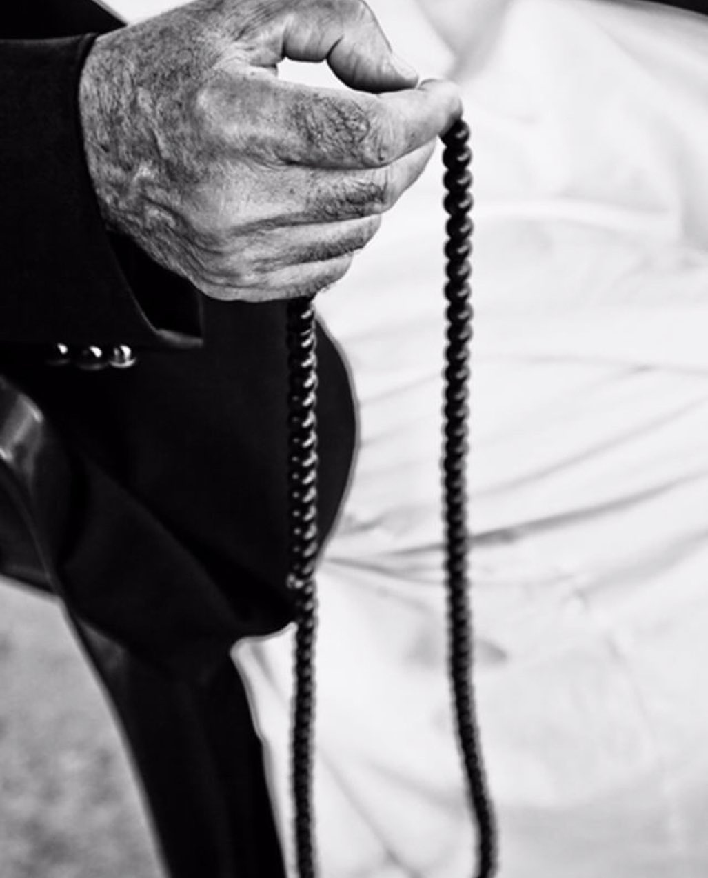 Close-up of an older man's hand holding prayer beads against a white robe — street photograph by Hamudi Leon