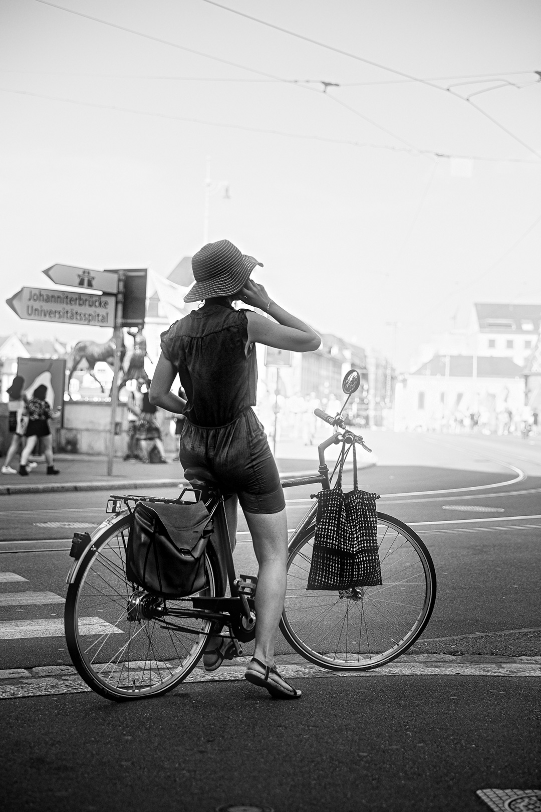 Woman in a sun hat waiting with a loaded bicycle at a crossing — street photograph by Hamudi Leon