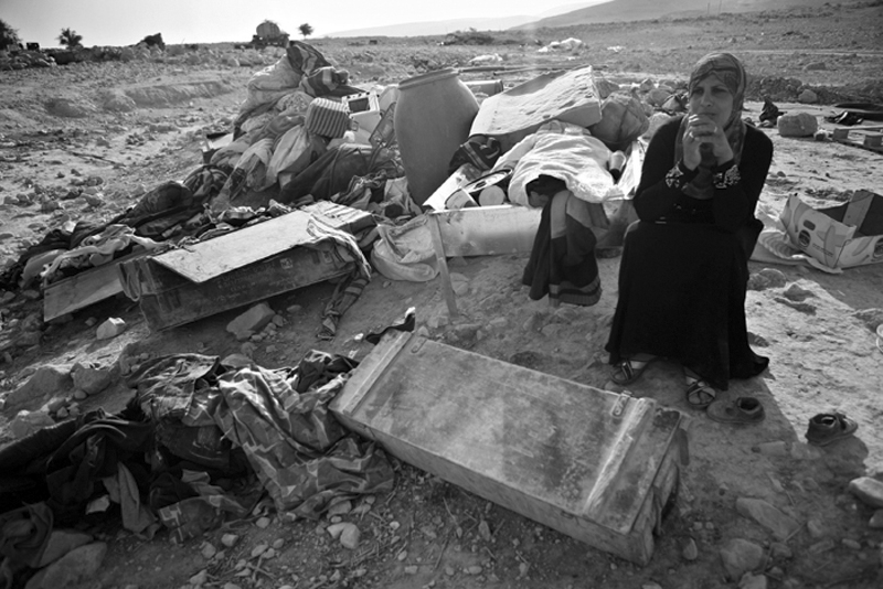 Woman sitting among scattered belongings on open ground — street photograph by Hamudi Leon