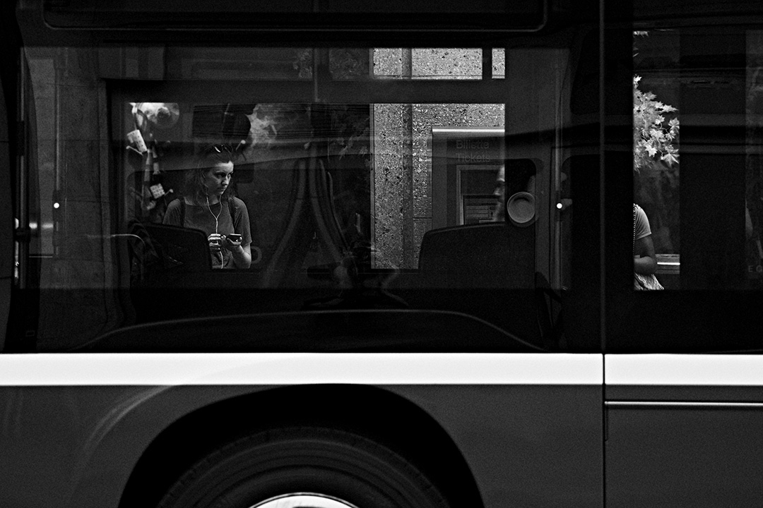 Passenger with a camera reflected in the window of a passing bus — street photograph by Hamudi Leon