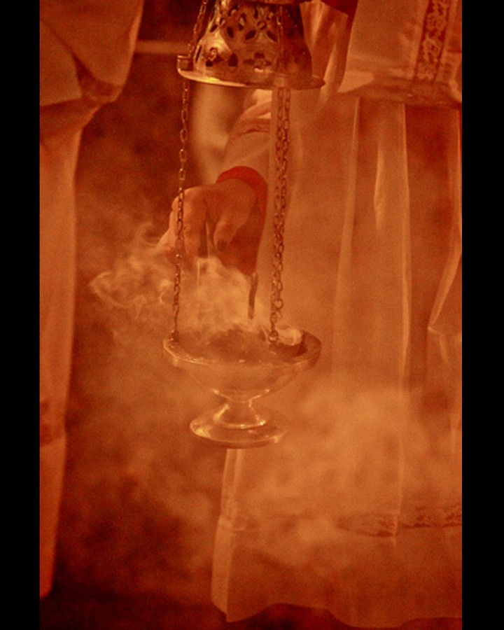 Glass censer hanging in orange smoke before a draped altar — street photograph by Hamudi Leon