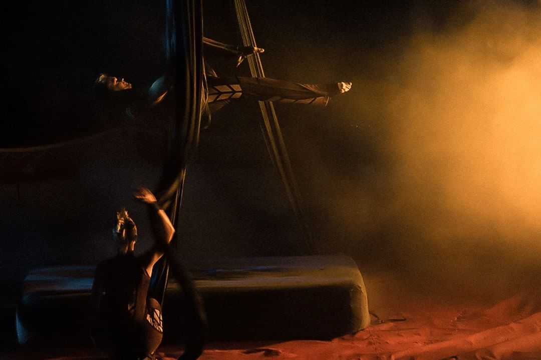 Performer on a stage in orange haze under a metal rig — street photograph by Hamudi Leon
