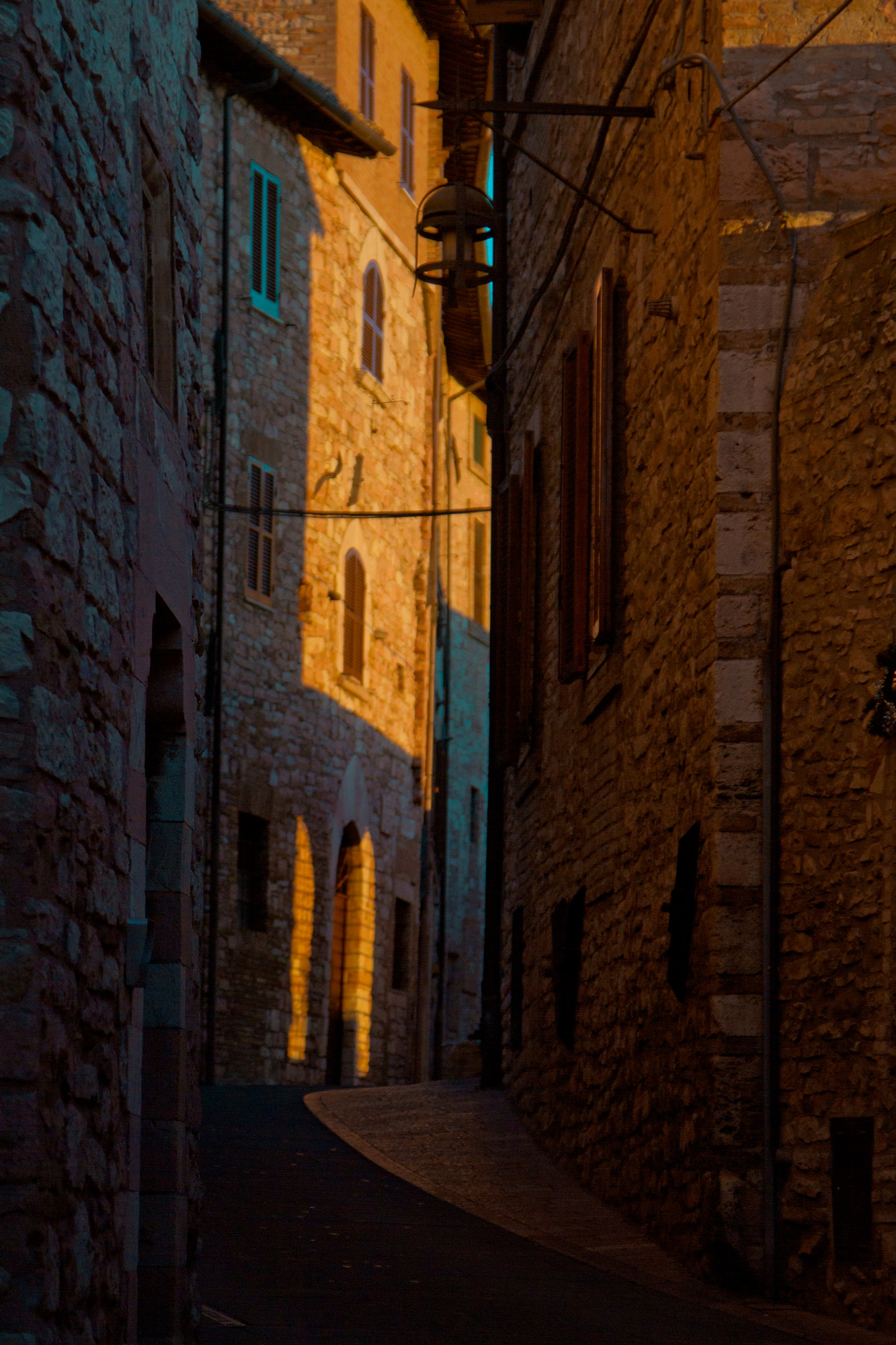 Narrow stone alley in evening light, lamps on the walls — street photograph by Hamudi Leon
